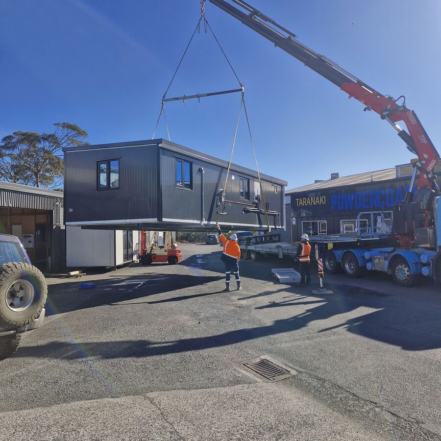 A hiab crane lifting a cabin off a truck in the yard